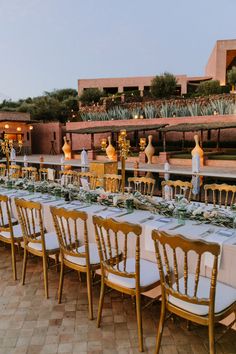 a long table is set up with white linens and gold chairs for an event