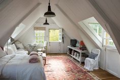 an attic bedroom is decorated in white and has a red rug on the hardwood floor