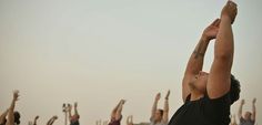 a group of people doing yoga outside with their arms in the air and hands up