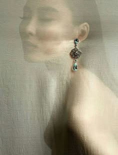 a woman's face is reflected in the glass behind her earring, which has a blue bead hanging from it