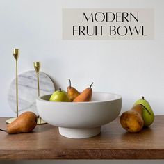 a white bowl filled with pears on top of a wooden table next to a mirror