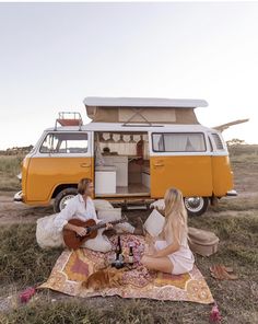 two people sitting on a blanket in front of an orange vw camper van