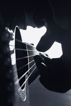 a person is playing an acoustic guitar in black and white with light coming through the strings