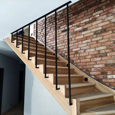 there is a brick wall behind the stair case and wooden handrails on this staircase