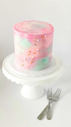 a pink and green cake with gold sprinkles sitting on top of a white cake stand