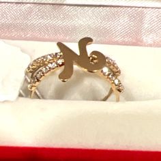 a gold ring with the letter k on it sitting in a red velvet box,