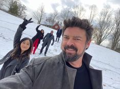 a man taking a selfie with his friends in the background on a snow covered hill