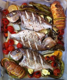 two fish and vegetables on a tray with lemons, tomatoes, peppers, and bread