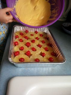 a person pouring batter into a pan with pineapples and cherries on it