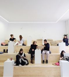 several people sitting on the steps in a room with white walls and wood floors, all looking at their phones