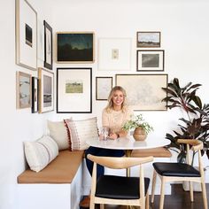 a woman sitting at a table in front of a bunch of pictures on the wall