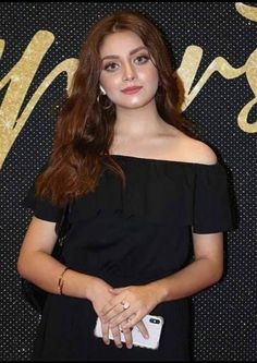 a woman standing in front of a black wall with gold writing on it and holding a white purse