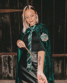 a woman dressed as harry potter holding a wand and wearing a green cape with hogwart's crest on it