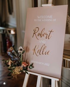 a welcome sign with flowers and greenery sits on an easel in a room