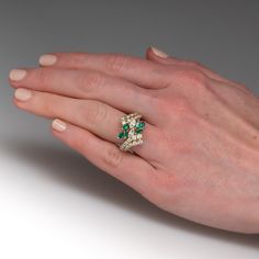 This pretty ring is centered with a cluster of two (2), prong set, marquise brilliant cut diamonds and six (6), prong set, marquise mixed cut natural emeralds. The top face of the by-pass style shank is accented with twenty-six (26), prong set, round brilliant cut diamonds. The ring measures 18.0mm at the top, rises 8.0mm above the finger, tapering to 2.9mm wide and 1.1mm thick at the base of the shank. This ring is currently a size 7. Luxury Marquise Emerald Ring With Prong Setting, Marquise Brilliant Cut Emerald Ring, Marquise Emerald Ring With Brilliant Cut, Green Marquise Brilliant Cut Rings, Fine Jewelry Emerald Ring With Marquise Brilliant Cut, Fine Jewelry Marquise Emerald Ring With Brilliant Cut, Marquise Emerald Ring For May Birthstone, Elegant Marquise Emerald Ring With Diamond Accents, Fine Jewelry Marquise Emerald Ring