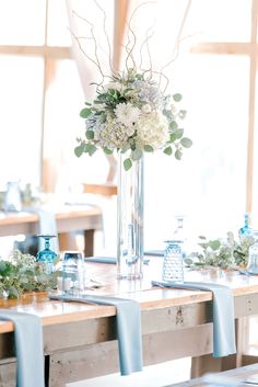 the table is set with blue chairs and white flowers in a tall vase on top