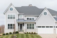 a white house with gray shingles and two garages on the side of it