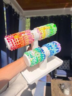 three colorful toothbrushes are being held by a person's hand in front of a window