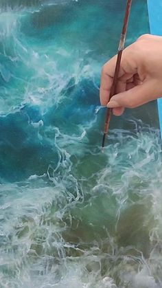 a person holding a paintbrush in their left hand and painting waves on a canvas