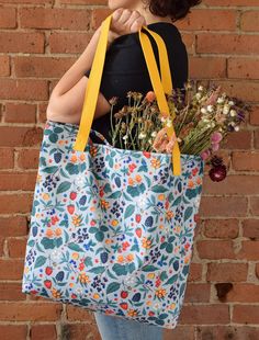 a woman is holding a large bag with flowers in it and the handles are yellow