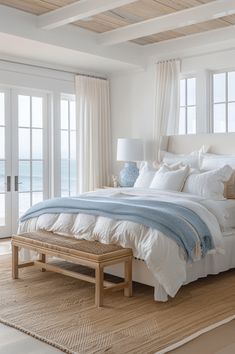 a bedroom with white walls and wooden floors, along with large windows that look out onto the ocean