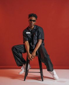 a man sitting on top of a stool wearing black pants and white sneakers with his legs crossed