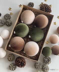 a box filled with different colored balls and pine cones next to christmas decorations on a white surface