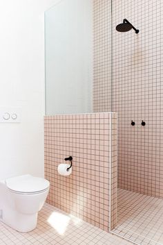 a white toilet sitting in a bathroom next to a walk in shower and tiled walls