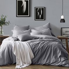 a bedroom with grey walls and pictures on the wall above it, along with a bed covered in gray sheets