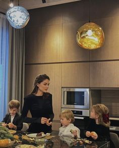 a woman standing in front of a kitchen counter filled with food and children sitting at a table