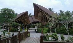 a wooden walkway leading to a building with large triangular shaped roof and trees in the background