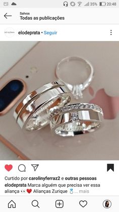 two silver rings sitting next to each other on top of a white table with an iphone in the background