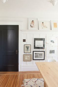 a room with pictures on the wall and a black door in the center, next to a wooden table