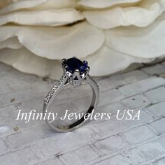 a blue diamond ring sitting on top of a white brick floor next to a flower