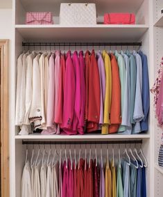 the closet is full of colorful clothes and handbags on hangers, including one pink purse