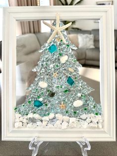 a christmas tree made out of sea glass and seashells in a white frame