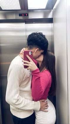 a man and woman kissing while standing in front of an open elevator door with their arms around each other