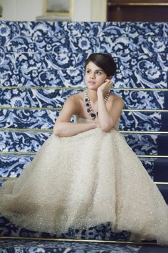 a woman in a white dress sitting on a blue and white chair with her hand under her chin