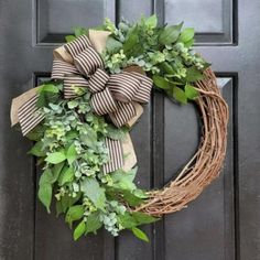 a wreath is hanging on the door with green leaves and ribbon tied around it's edges