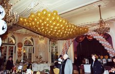 two men standing in front of a bar with balloons on the ceiling and chandeliers hanging from the ceiling