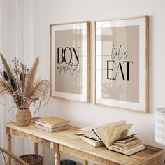 two framed posters on the wall above a wooden table with books and plants in vases