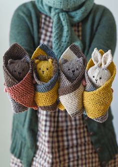 a woman holding four knitted animals in her hands, all wearing sweaters and scarves