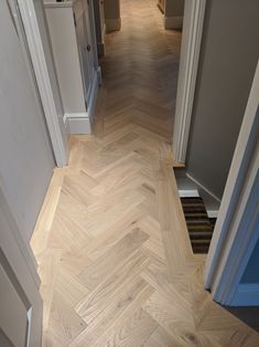 an empty hallway with wood flooring and white trim on the walls, leading to another room