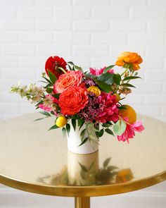 a vase filled with colorful flowers sitting on top of a gold table next to a white brick wall