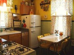 a kitchen with a table, stove and refrigerator in the corner next to two windows