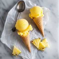 three scoops of ice cream with pineapple slices on a marble counter top next to a spoon