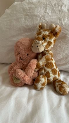 two stuffed giraffes sitting next to each other on a bed