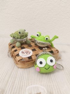 two green stuffed animals sitting on top of a wooden basket next to another one with eyes