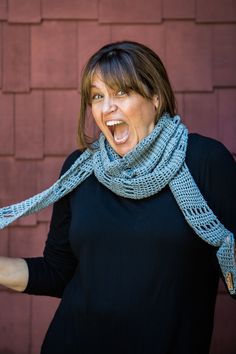 a woman with her mouth wide open wearing a blue knitted scarf and black shirt