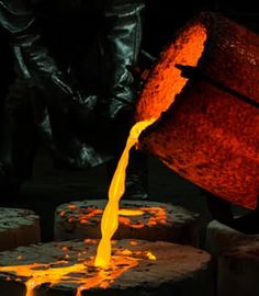 a person pouring orange liquid into a bucket on top of bricks in an industrial setting